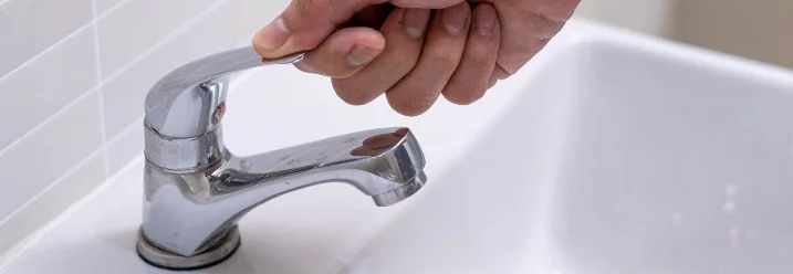 Hand dreht Wasserhahn auf